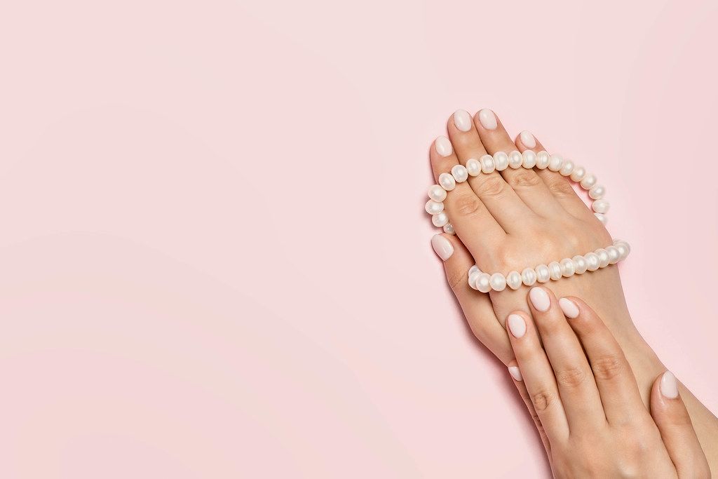 An unrecognizable woman hands with cute manicure holding pearls necklace bright pink background. Manicure and beauty concept (Flip 2020)