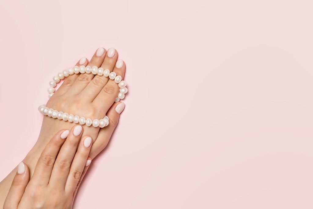 An unrecognizable woman hands with cute manicure holding pearls necklace bright pink background. Manicure and beauty concept