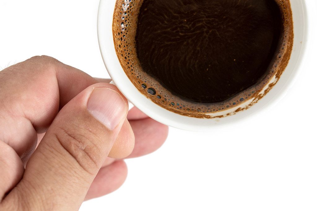 Ansicht von oben auf eine Tasse mit schwarzem Kaffee in einer Hand, vor weißem Hintergrund