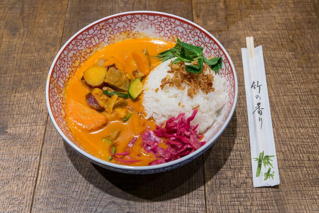 Asiatisches Wok & Bowl Essen im Coa Restaurant: Red Hot Chili Curry mit Rindfleisch, Süßkartoffeln, Gemüse und Reis, neben Essstäbchen