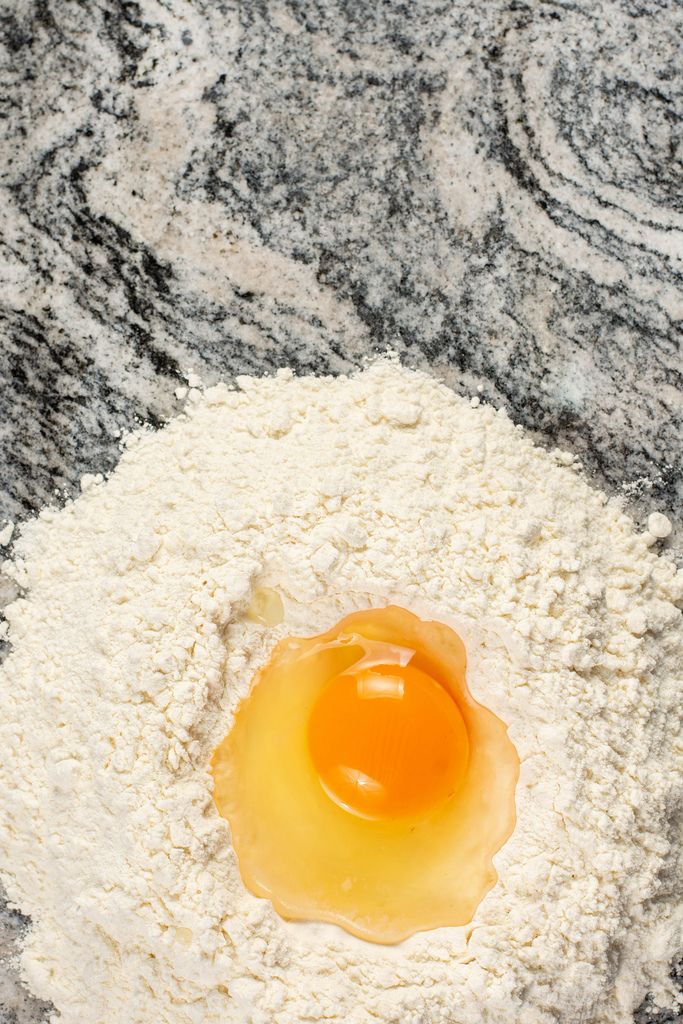 Aufgeschlagenes Ei in Mehlhaufen blank auf Marmorplatte