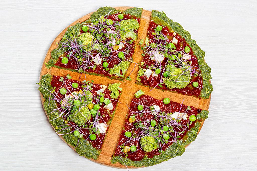 Aufnahme von oben von Pizza mit Mini-Brokkoli und anderen Gemüsesorten vor weißem Hintergrund