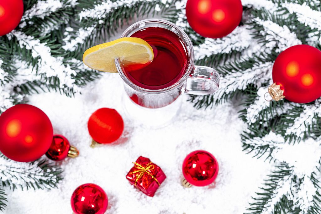 Aufsicht auf ein Glas Glühwein mit Weihnachtsbaumkugeln und Tannenzweigen im Schnee