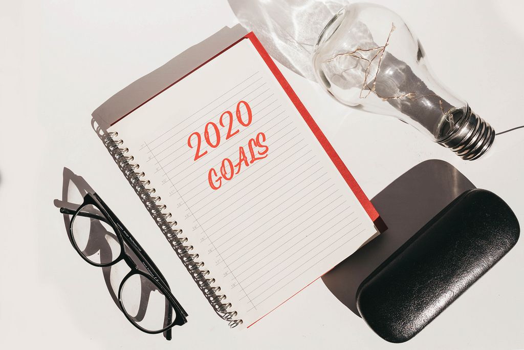 Aufsicht tauf Schreibtisch mit Notizbuch - Ziele 2020 - Brille und Glühbirne