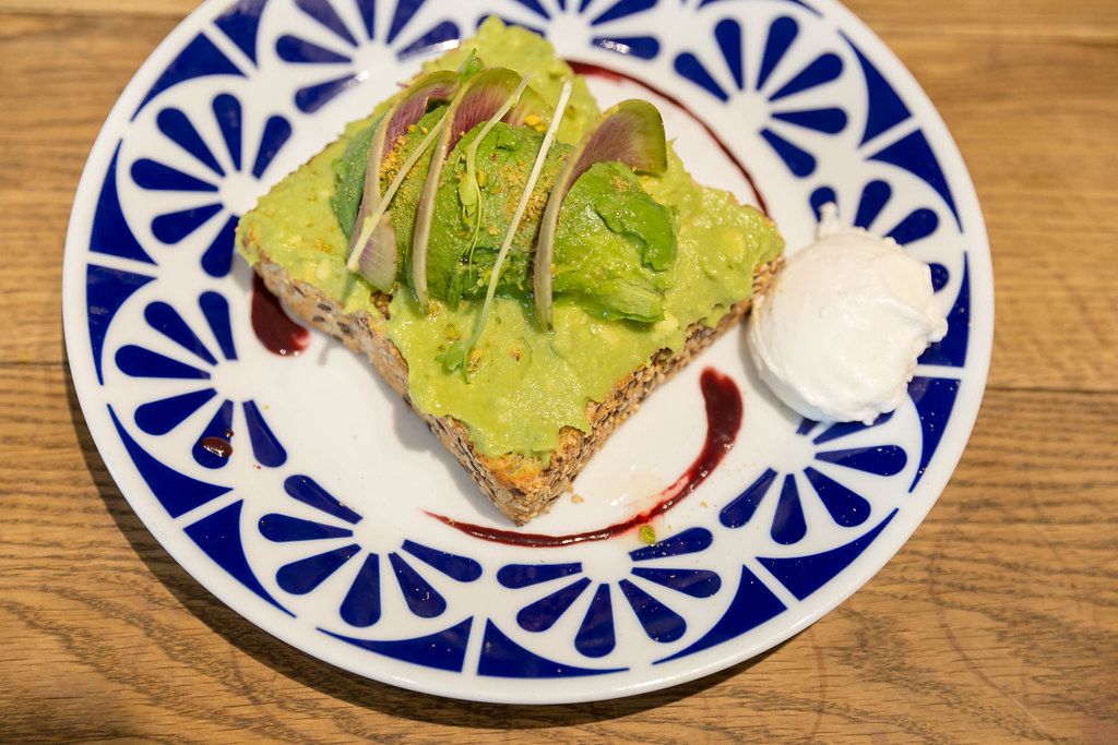 Avo-Toast from whole wheat sliced bread with guacamole, pistachio, yuzu & açai sauce, nutritional yeast and poached egg in Flax&Kale in Barcelona, Catalonia