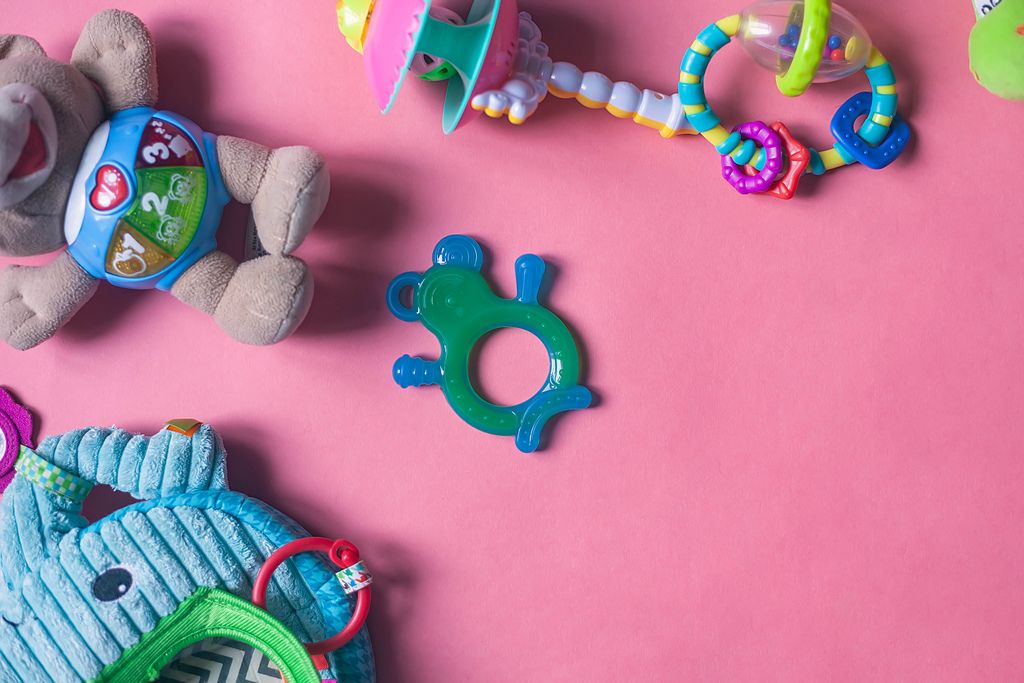 Baby-Spielzeuge wie Babyrassel, Beißring und Plüschtiere auf rosarotem Hintergrund