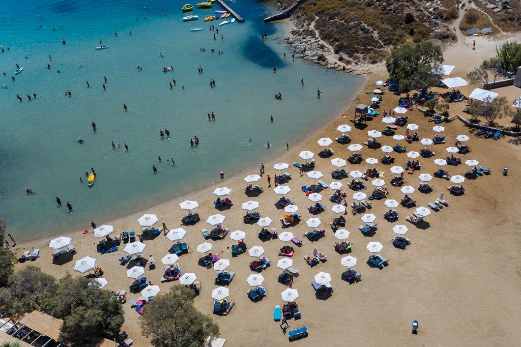 Badegäste im Mittelmeer und auf Strandliegen, unter weißen Sonnenschirmen, am weißen Sandstrand Monastiri auf Paros