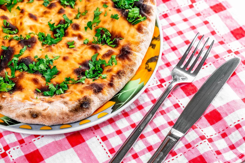 Baked khachapuri with parsley and cheese on the table with knife and fork (Flip 2019)