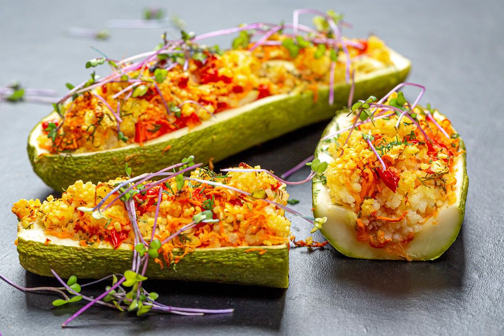 Baked zucchini with vegetables and couscous on a black background with micro green cabbage