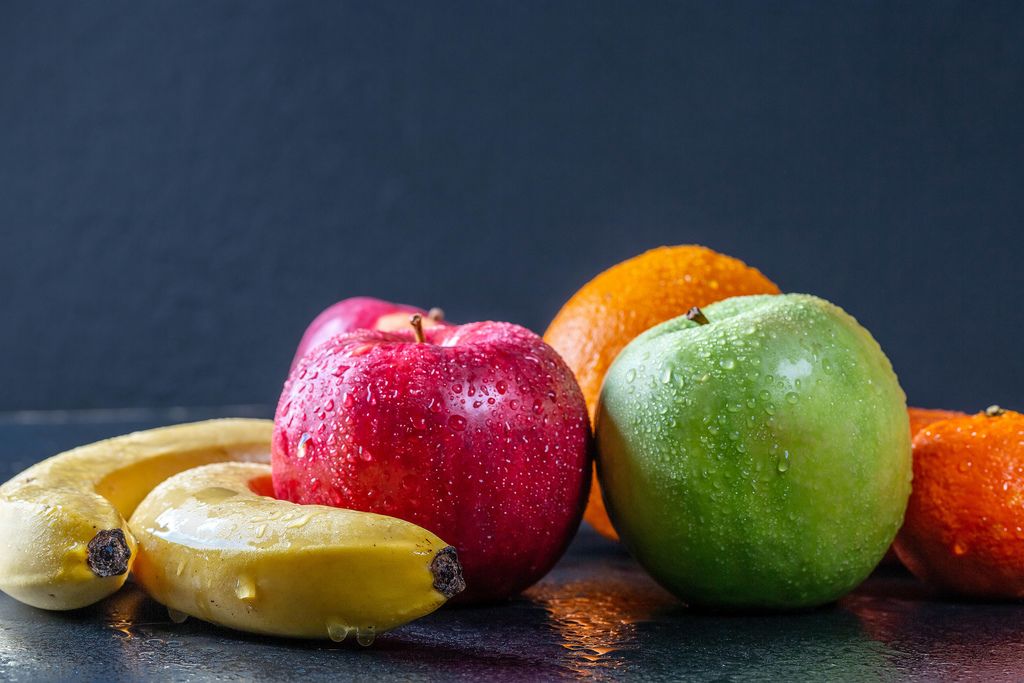 Bananas, apples and citrus with water droplets on black background