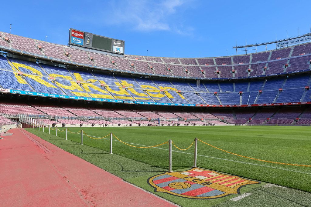 Barrier chain at the soccer field of the Camp Nou stadium and FC Barcelona team logo, with blue-purple tribune in the background, in Spain