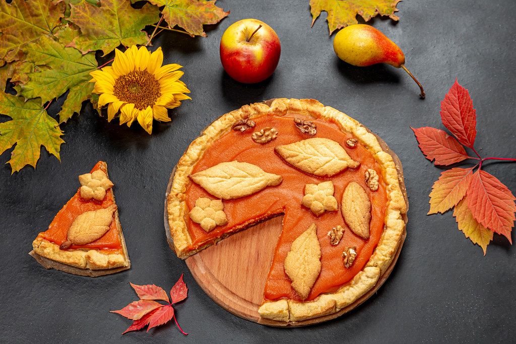 Beautiful decorated pumpkin pie on black background with autumn leaves, apple and sunflower flower (Flip 2019)