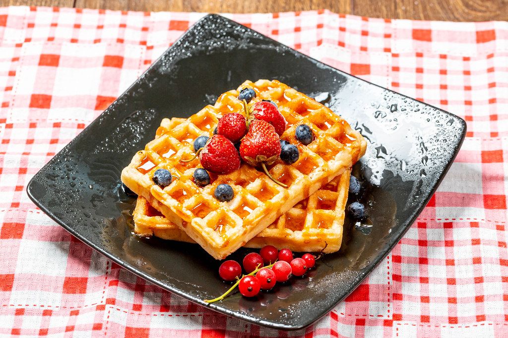 Belgian waffles with blueberries, strawberries and red currants on a black plate