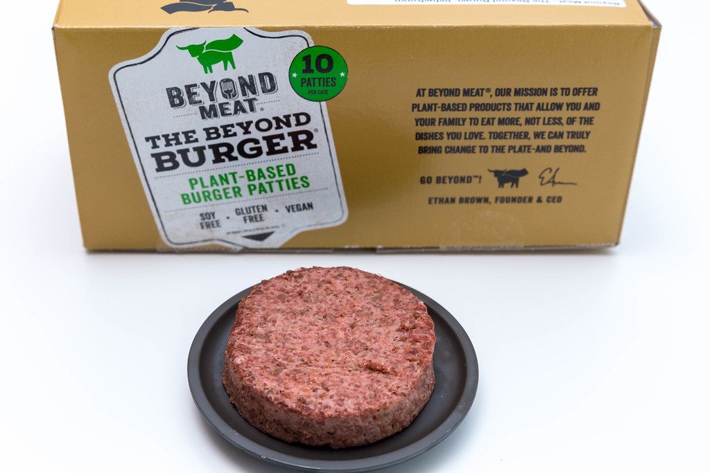 Beyond Meat Patty - eine vegane, glutenfreie Alternative zum Burger-Fleisch - auf schwarzem Teller mit der Packung im Hintergrund