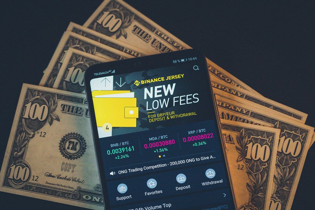 Binance Kryptopwährungs-Wechsel App auf einem Handydisplay mit einhundert Dollarnoten