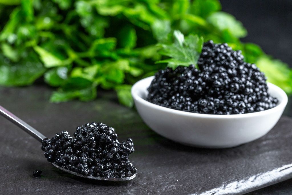 Black caviar on a dark stone background with greens (Flip 2019)