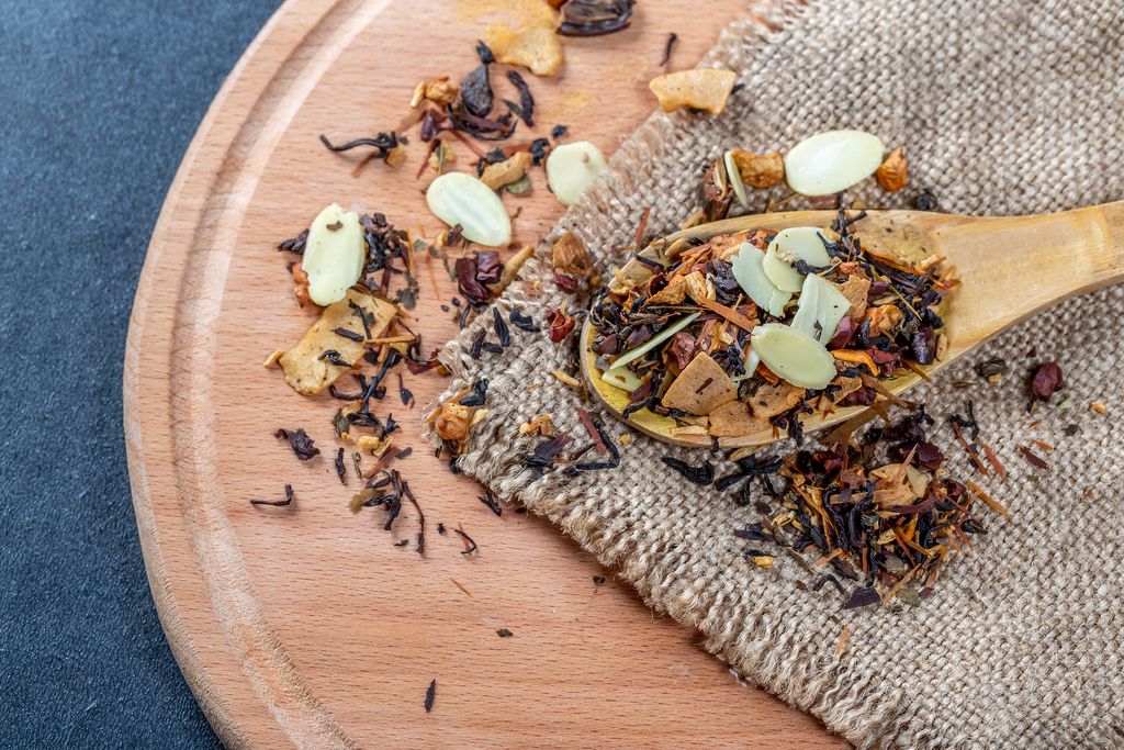 Black tea with dried fruits and pieces of different nuts in a spoon on the burlap