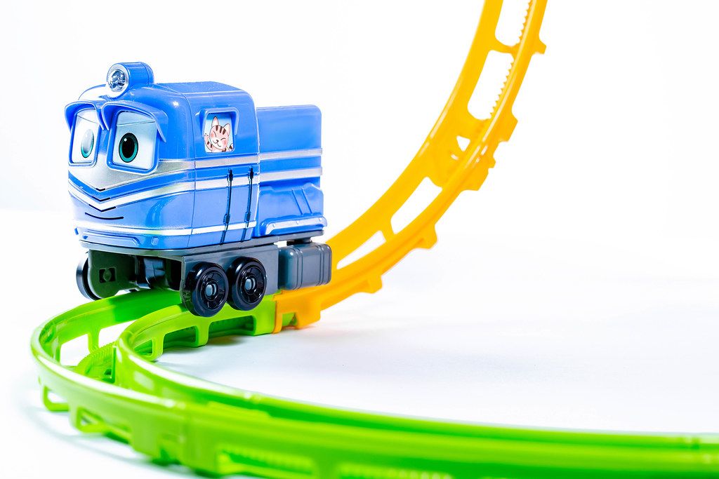 Blaue Spielzeugeisenbahn auf bunten Plastikschienen vor weißem Hintergrund