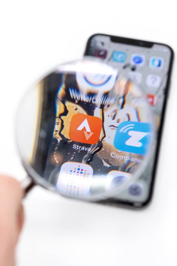 Blick durch Lupe auf Strava App auf schwarzem Mobiltelefon vor weißem Hintergrund