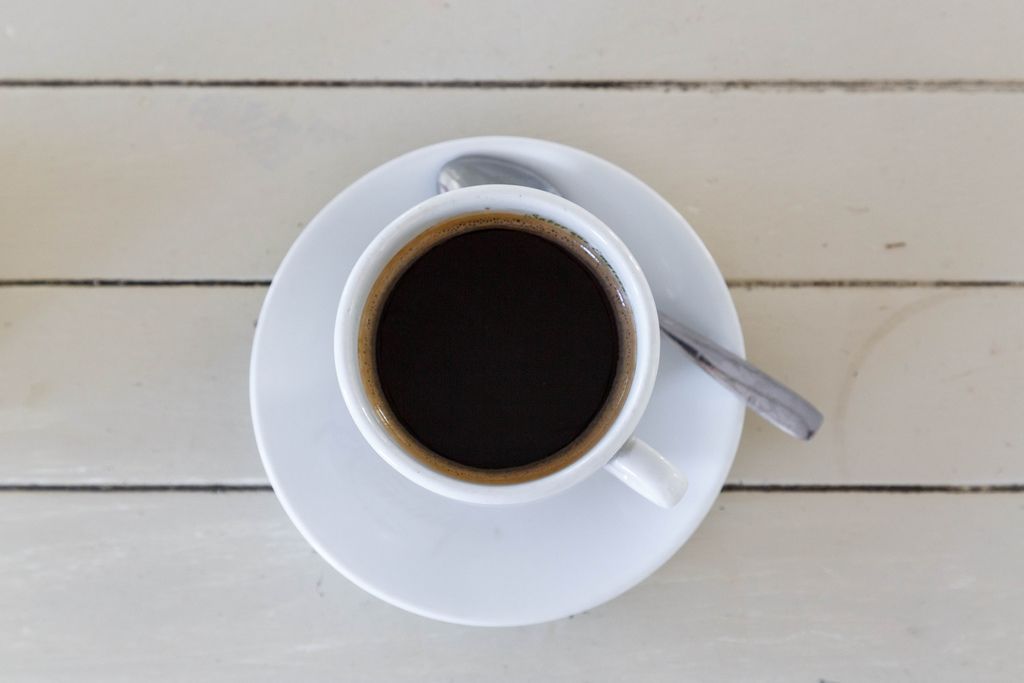 Blick von oben auf eine weiße Tasse gefüllt mit Americano Kaffee auf weißem Holzhintergrund