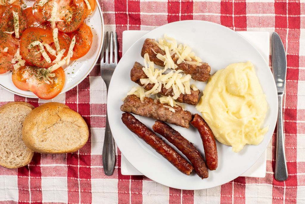 Blick von oben auf Gericht mit Hackfleischwürste, Stampfkartoffeln, knuspriges Brot und Tomaten