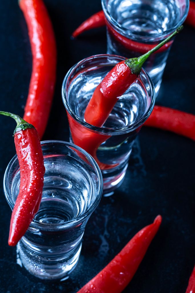 Blick von oben auf Gläser gefüllt mit Wodka und scharfen frischen Chilis auf schwarzem Tisch
