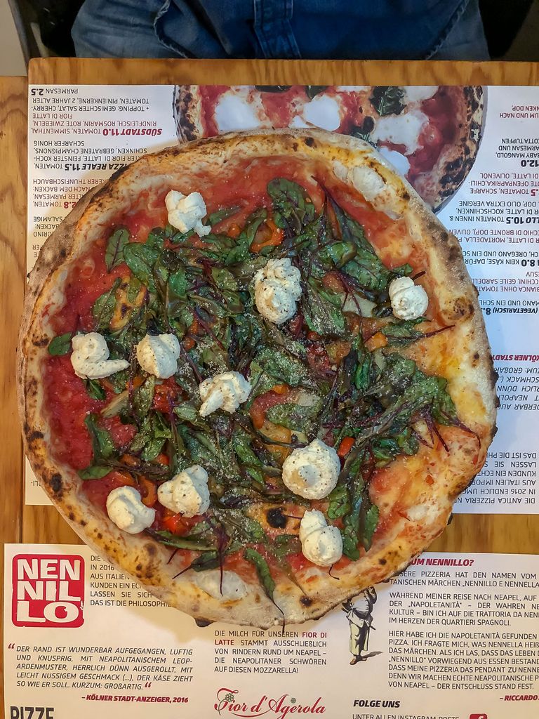Blick von oben auf reichhaltige Pizza mit Käse und Kräutern auf Tischset mit Menu in Pizzeria