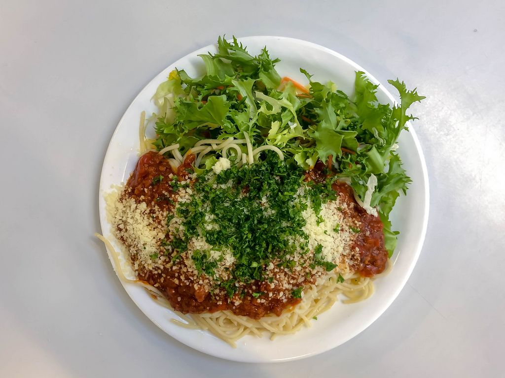 Blick von oben auf Teller Spaghetti mit Tomatensoße, geriebenem Käse, Petersilie und grünem Salat