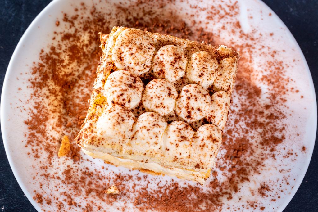 Blick von oben auf Tiramisu-Dessert mit Schokopulver angerichtet auf weißem Teller