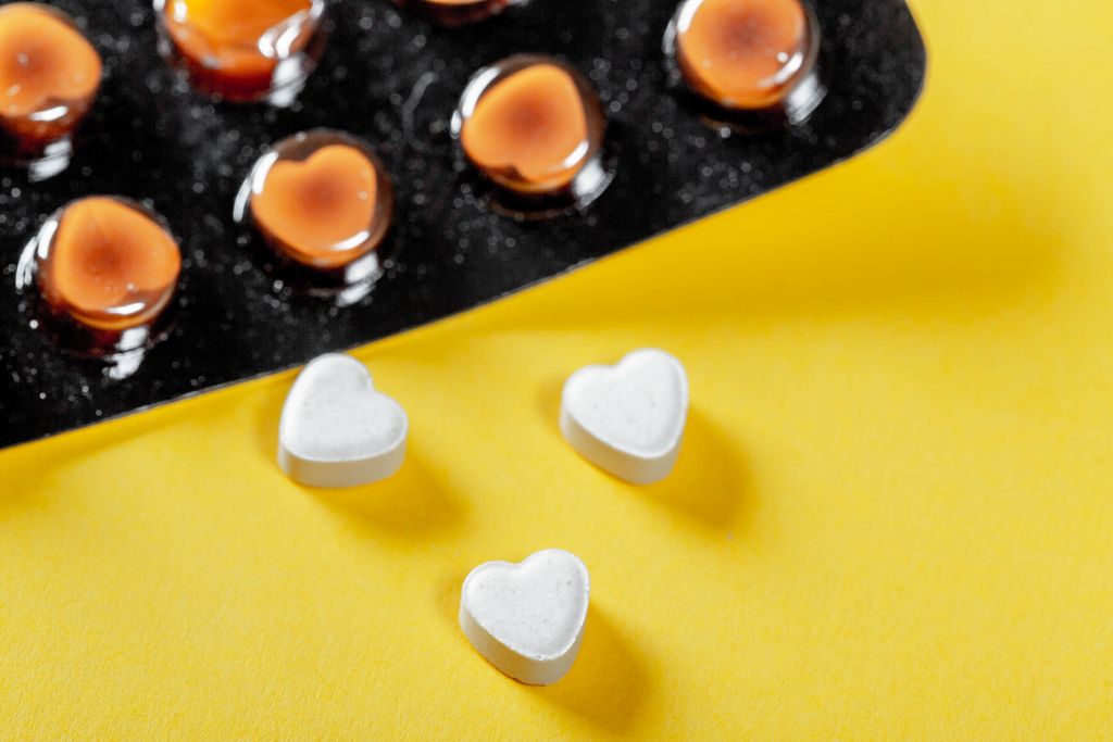 Blister-Packung mit Medikamenten und drei Tabletten in Herzform auf gelbem Hintergrund