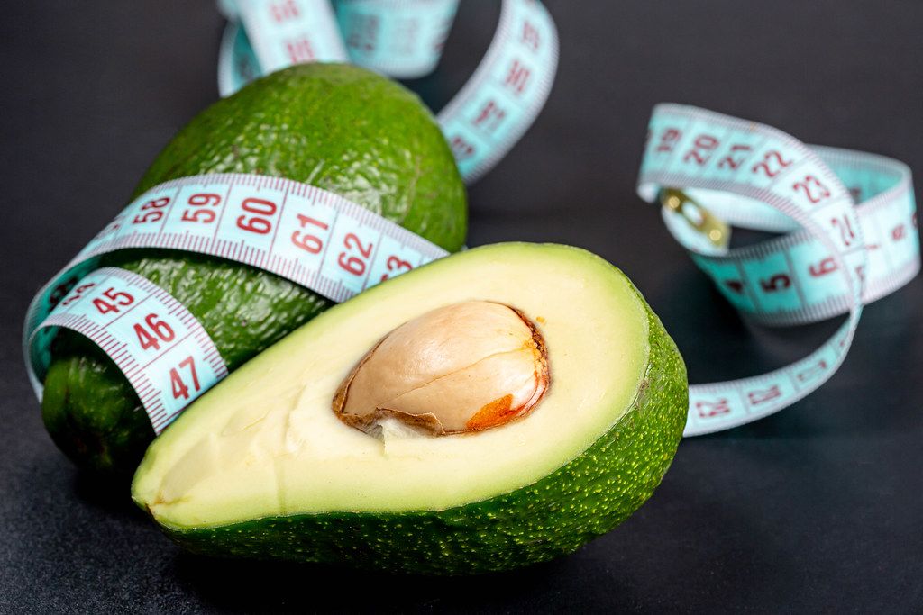 Body care and proper nutrition. Fresh avocado and measuring tape on black