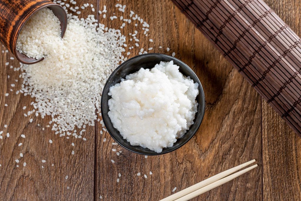 Boiled and raw Chinese rice in a bowl on a wooden table with chopsticks (Flip 2019)