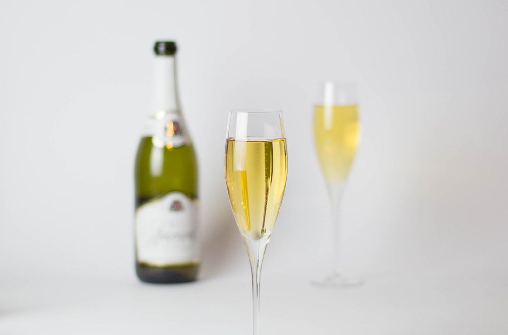 Bokeh Photo of Full Champagne Glass with Champagne Bottle and other Glass in the Background for Celebrations