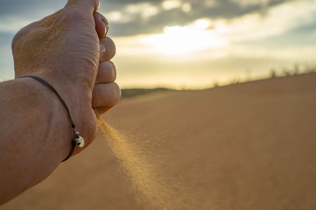 Bokeh Shot of a Hand dropping Sand in the Desert with Sunset in the Background