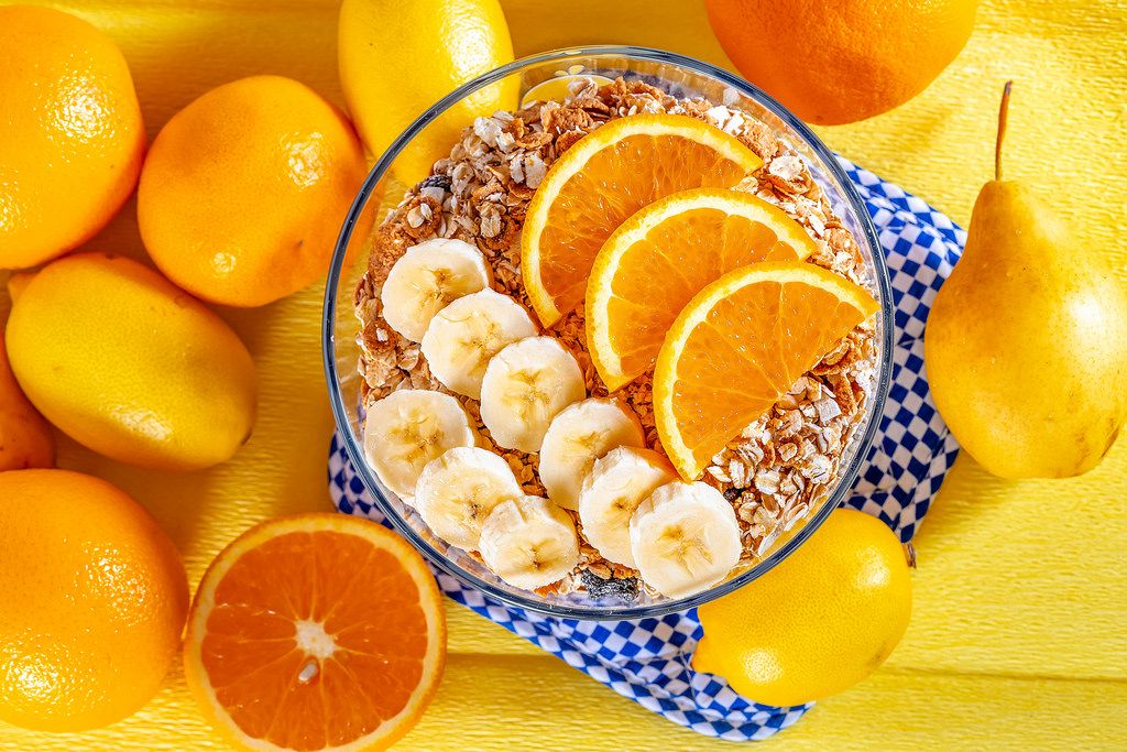 Bowl of cereal with bananas and oranges for Breakfast on fresh fruit background