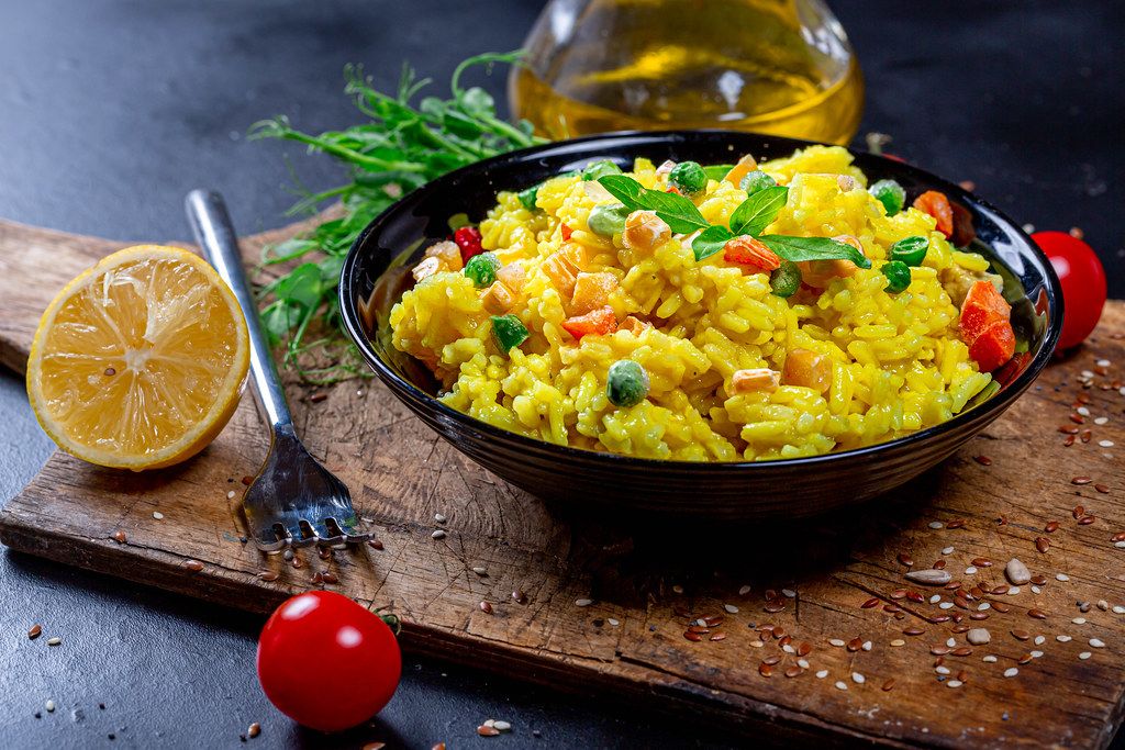 Bowl of yellow rice with vegetables and greens on a dark background with olive oil, tomatoes and seeds