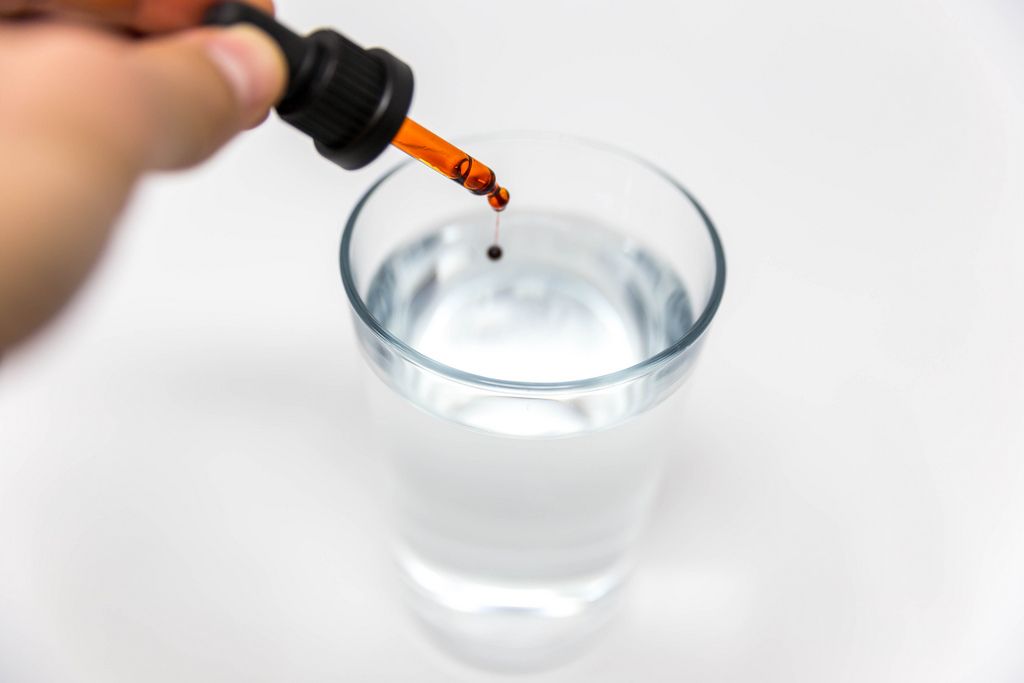 Braineffect Recover CBD Öl träufelt einen einzelnen Tropfen aus der Pipette in ein Wasserglas