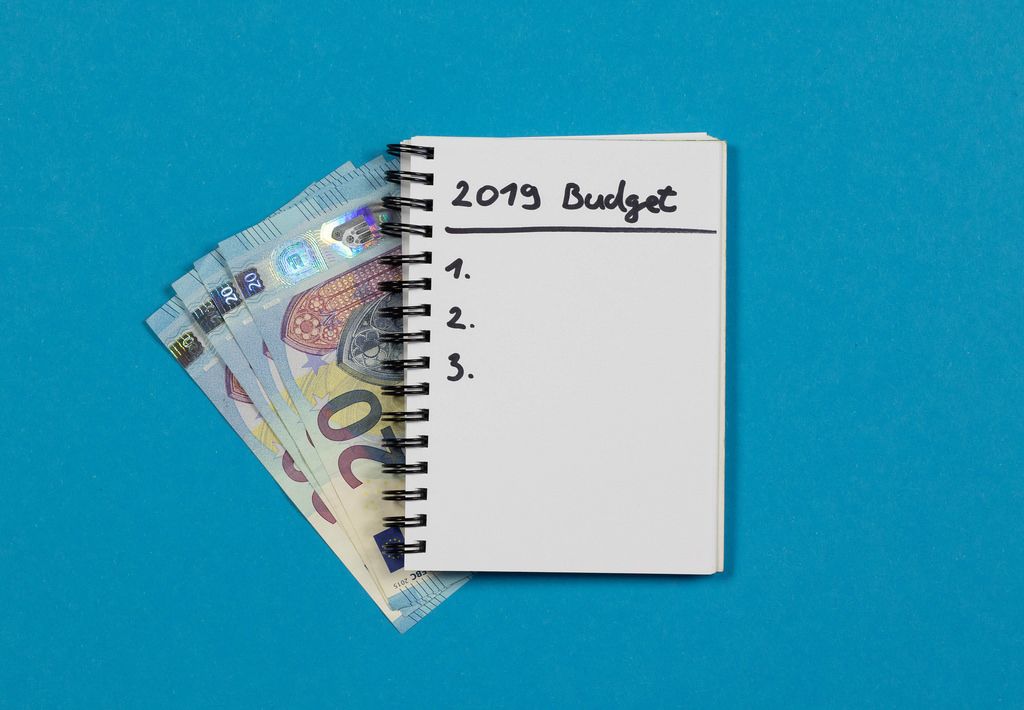 Budget Berechnung für das Jahr 2019 - Spiralheft mit Liste und Geld auf blauem Hintergrund