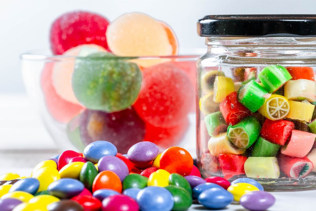 Bunte Süßigkeiten und Bonbons in Gläsern und auf Tisch vor weißem Hintergrund