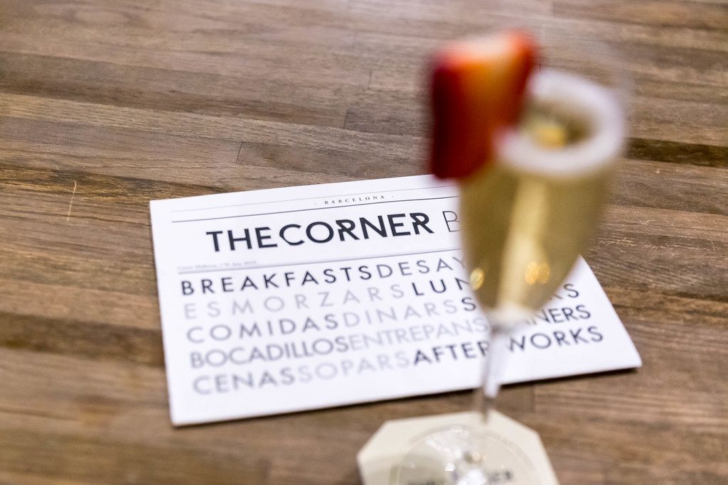 Business card of The Corner Bar advertised breakfast and snacks, next to a blurred champagne glass with strawberry slice , in Barcelona (Spain)