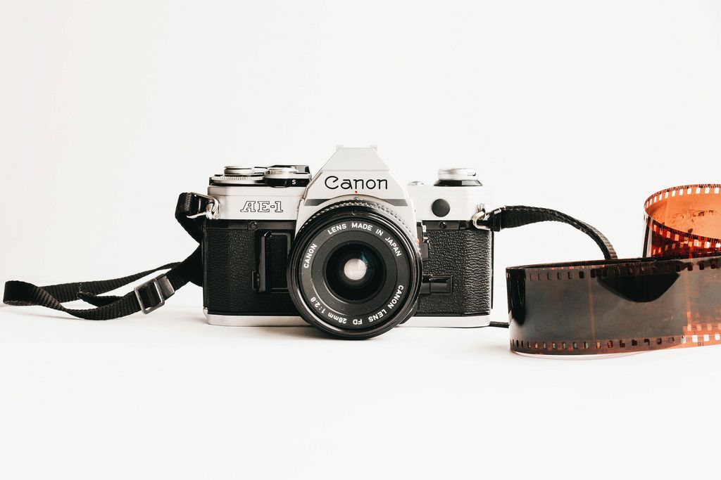 Canon AE-1 film camera and roll of developed film on white background