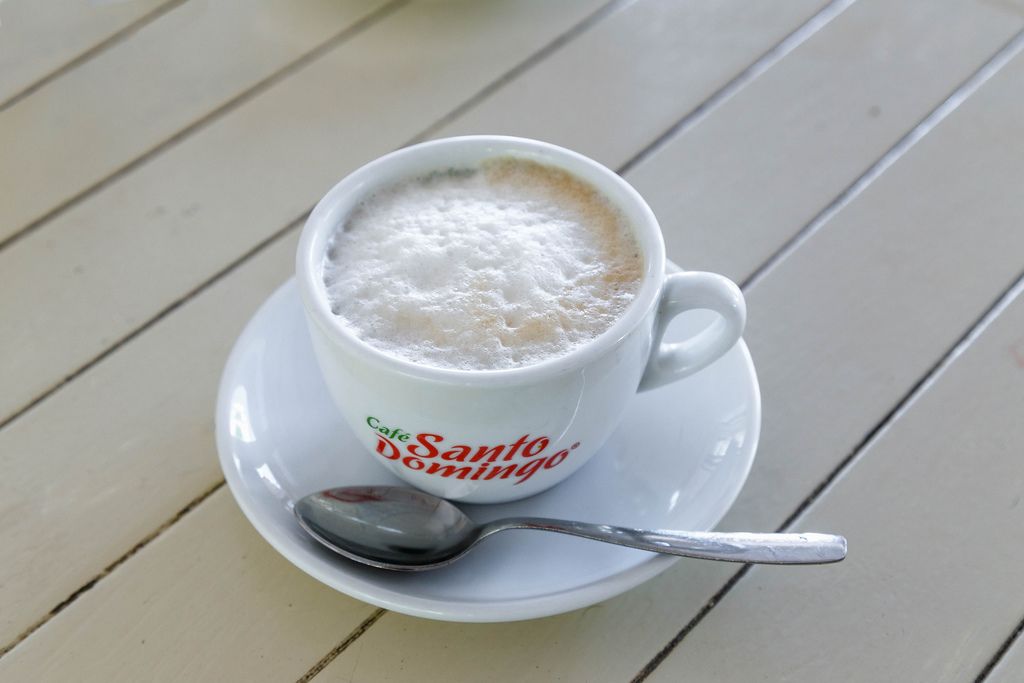 Cappuccino mit Milchschaum in weißer Tasse mit Löffel auf weißem Hintergrund aus Holz