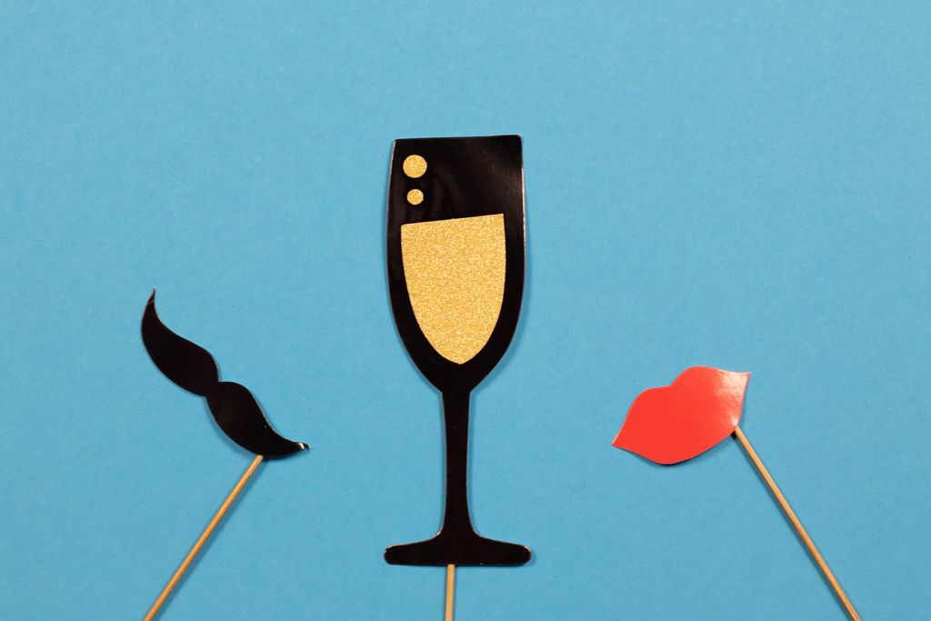 Champagnerglas mit Schnurrbart und Lippen aus Papier auf blauem Hintergrund - Hochzeitsspiel