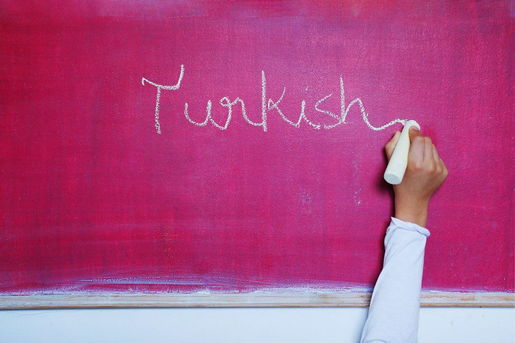 Child writes Turkish word on chalkboard, learning foreign language