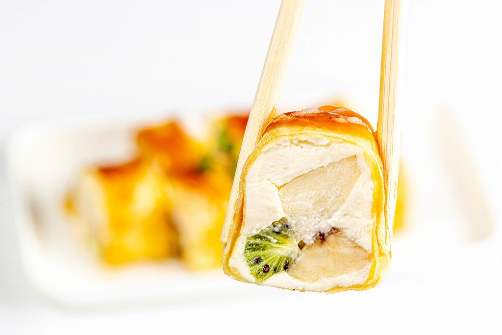 Chopsticks hold a dessert roll with cheese, Apple, kiwi and banana
