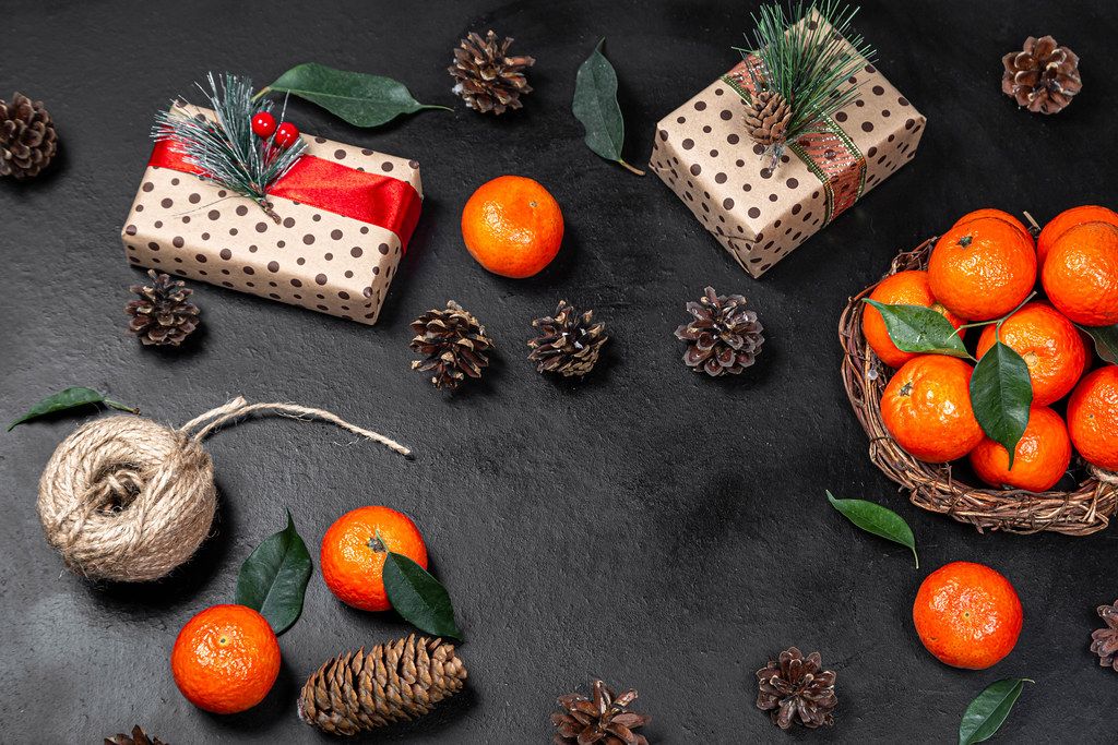 Christmas gifts with tangerines and cones on a black background. The view from the top