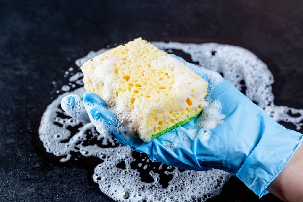 Cleaning the house concept: hand holding a yellow sponge wet with foam on a black background