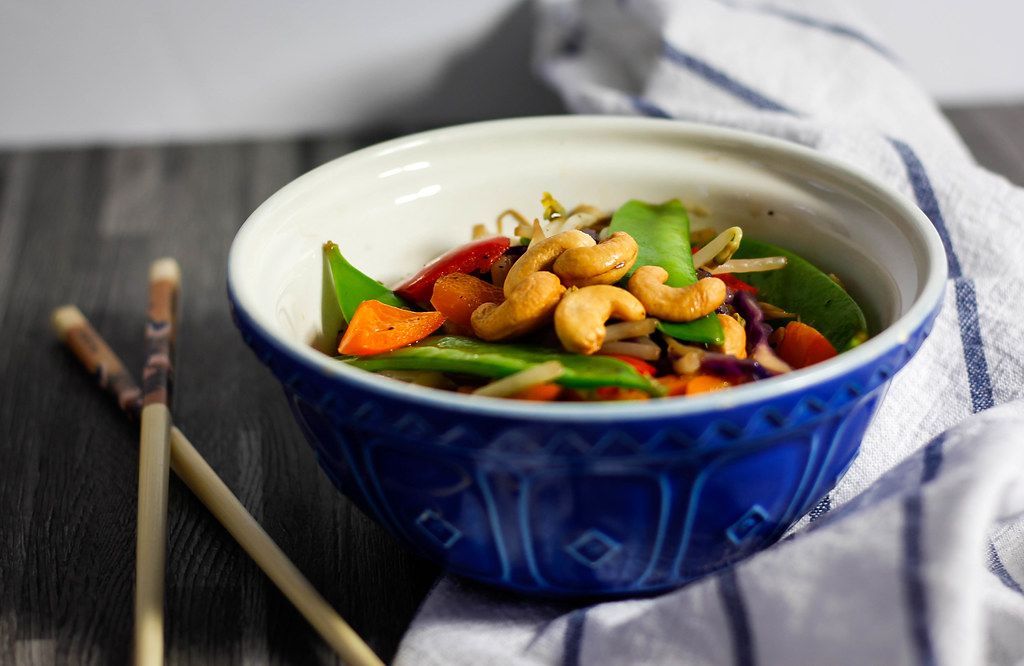 Close Up Food Photo of Asian Stir-Fried Vegetables with Cashew Nuts in Bowl next to Chopsticks on Wooden Table