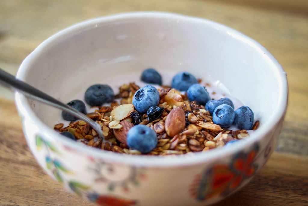 Close Up Food Photo of Healthy Granola Breakfast Bowl with Almonds and Blueberries in Ceramic Bowl on Wooden Table