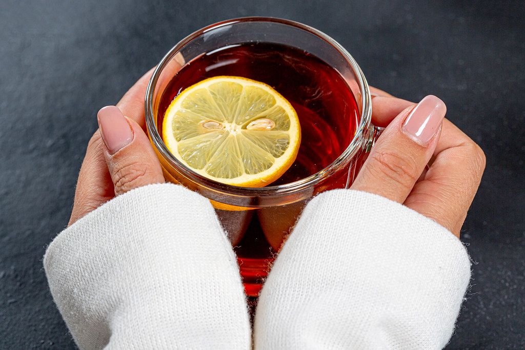 Close-up of a Cup of black tea with a piece of lemon in women's hands